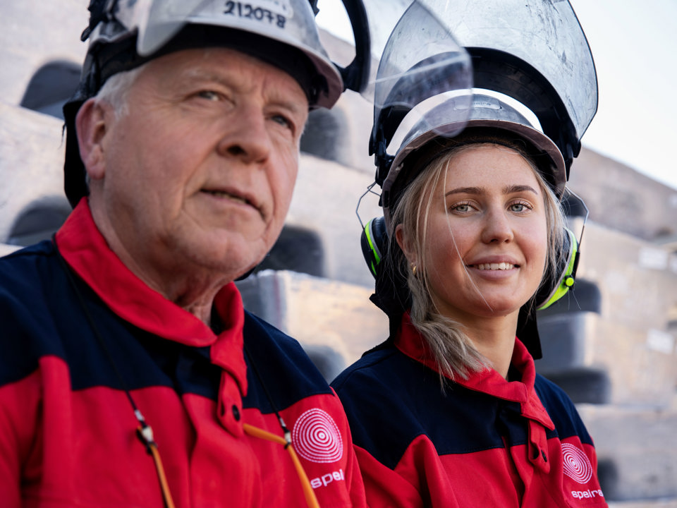 Two smiling Speira employees in work clothes leaning on aluminum bars.
